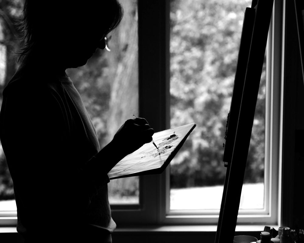 Silhouette of a person holding a paint palette in front of a window with natural light.